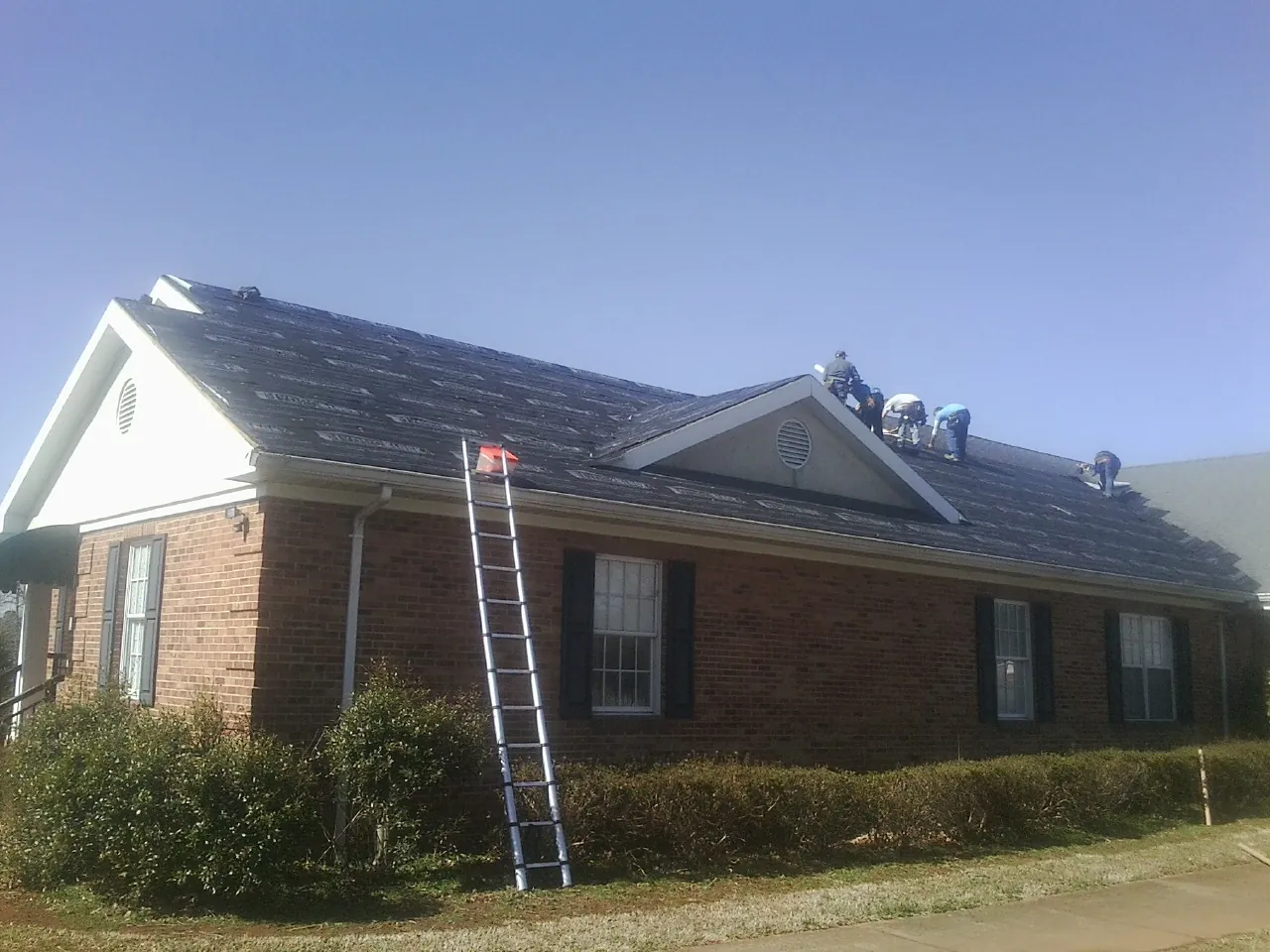 Crew tearing shingles off a brick ranch roof with a ladder set — Metal Roof Repair work by our crew in Wharton