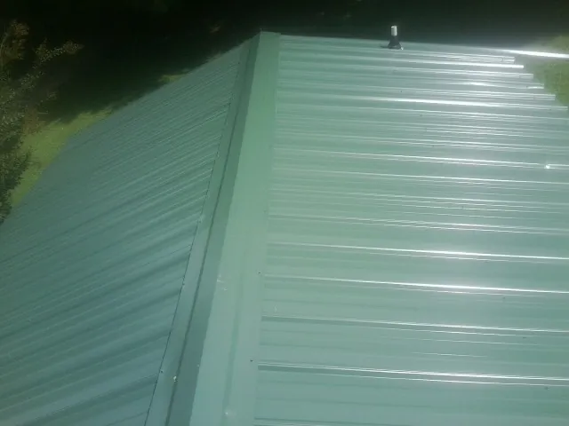 New green metal panels meeting at the ridge of a roof — Flat Roof Repair work by our crew in Wharton